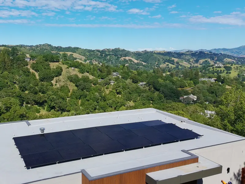 Black solar panels on a light gray flat roof, with green hills behind