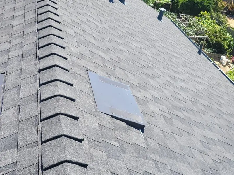A gray shingle roof with ridge cap, vents and a skylight