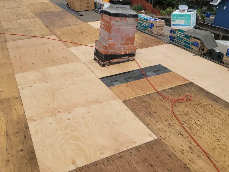 Roof deck around a brick chimney, with new plywood sheets beside older boards