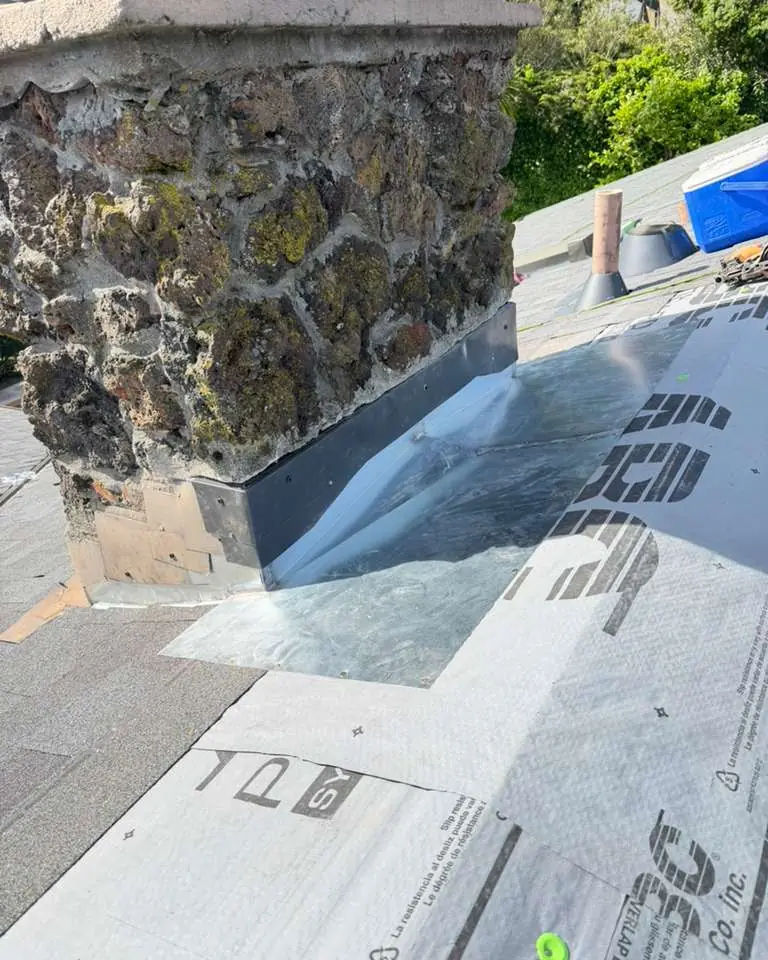 New metal flashing at the base of a stone chimney, over the underlayment